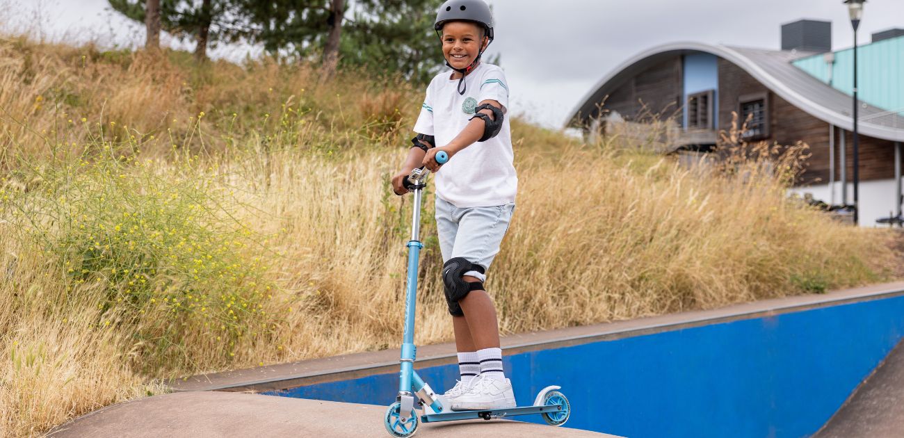 A young boy at a skatepark, smiling and posed with a blue Osprey skateboard