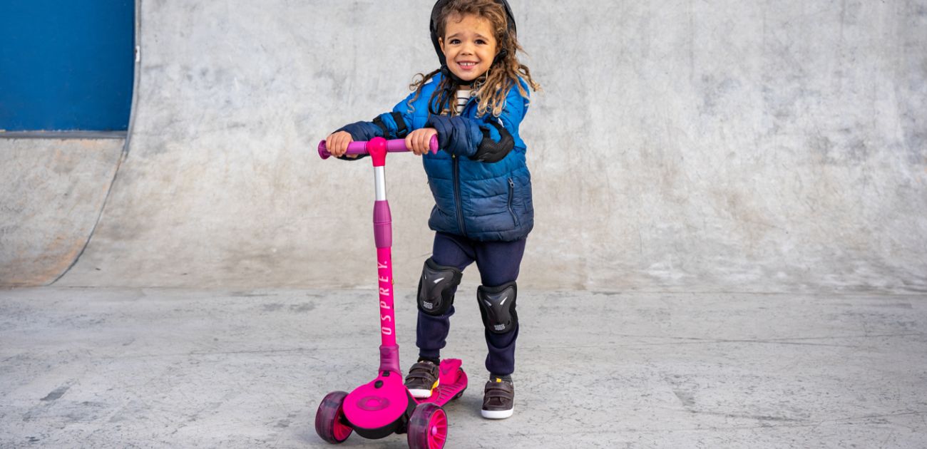 a young boy riding a pink three wheeled scooter