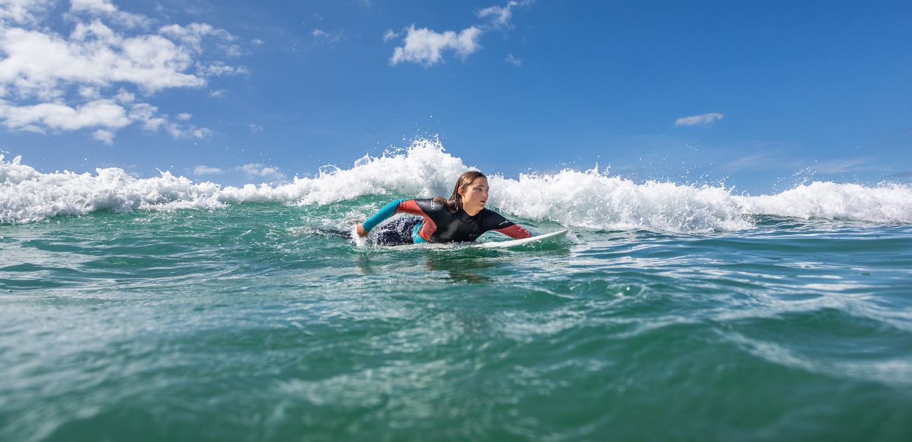 a women paddling on a surfboard in clear blue sea and a blue cloudy sky