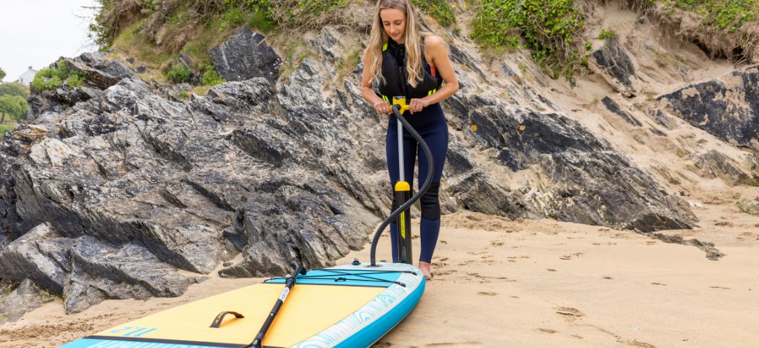 A photo of a woman on the beach pumping up her SUP