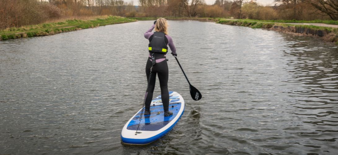 A photo of a woman paddleboarding on a river in Autumn