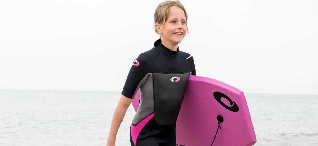 a photo of a girl on the beach in an Osprey wetsuit carrying a bodyboard