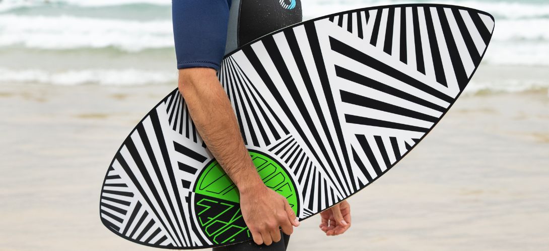 A photo of a man carrying a black and white striped skimboard under his arm