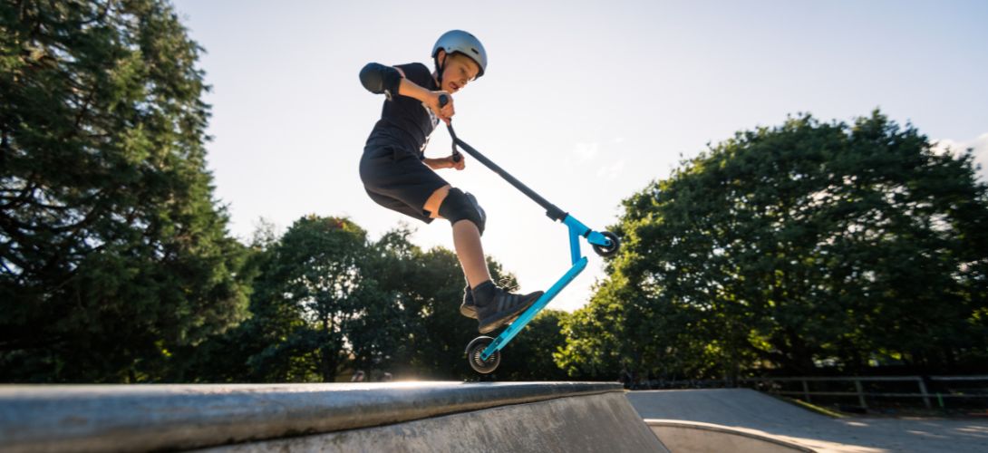 A photo of a boy performing a trick in the air on a blue stunt scooter