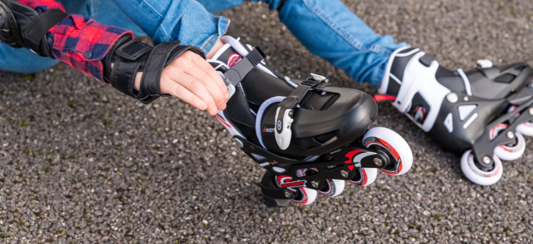 A close up photo of a boy adjusting the fastening on a pair of black and red Osprey inline skates