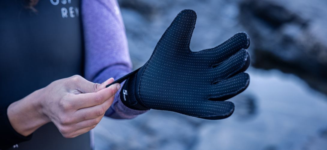 A close up photo of a woman putting on a blacks neoprene glove